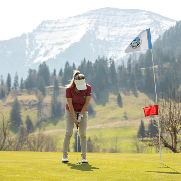 Golferin beim Einlochen auf dem Green am Golfplatz Steibis mit Hochgrat Panorama