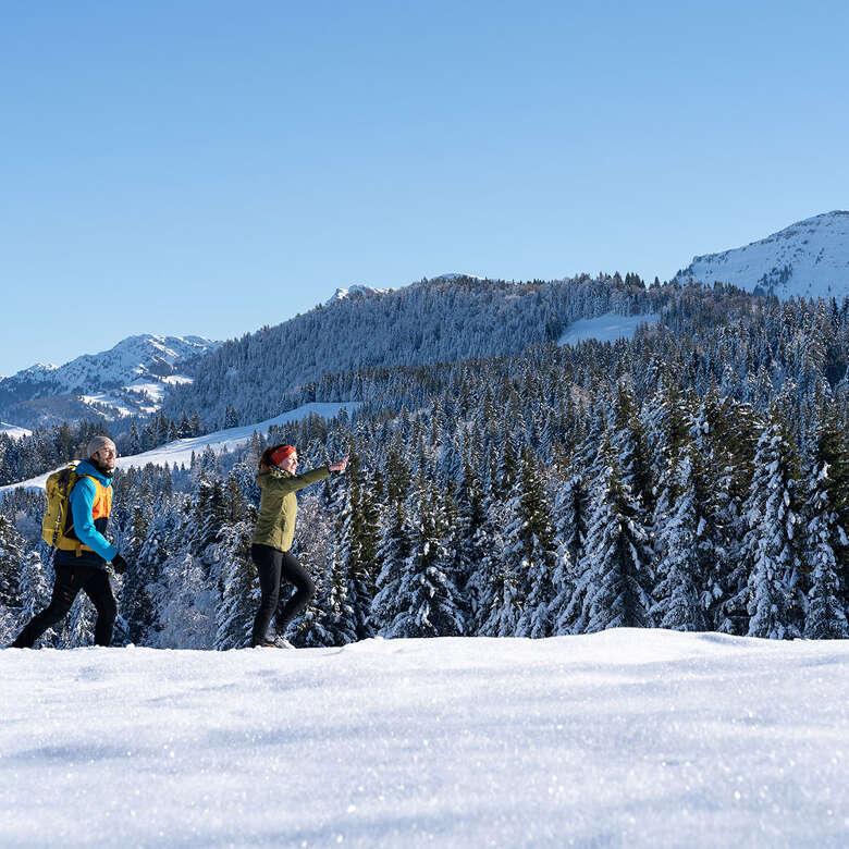 Winterwandern im Schnee von Oberstaufen mit Blick auf die verschneiten Wälder und Berge.