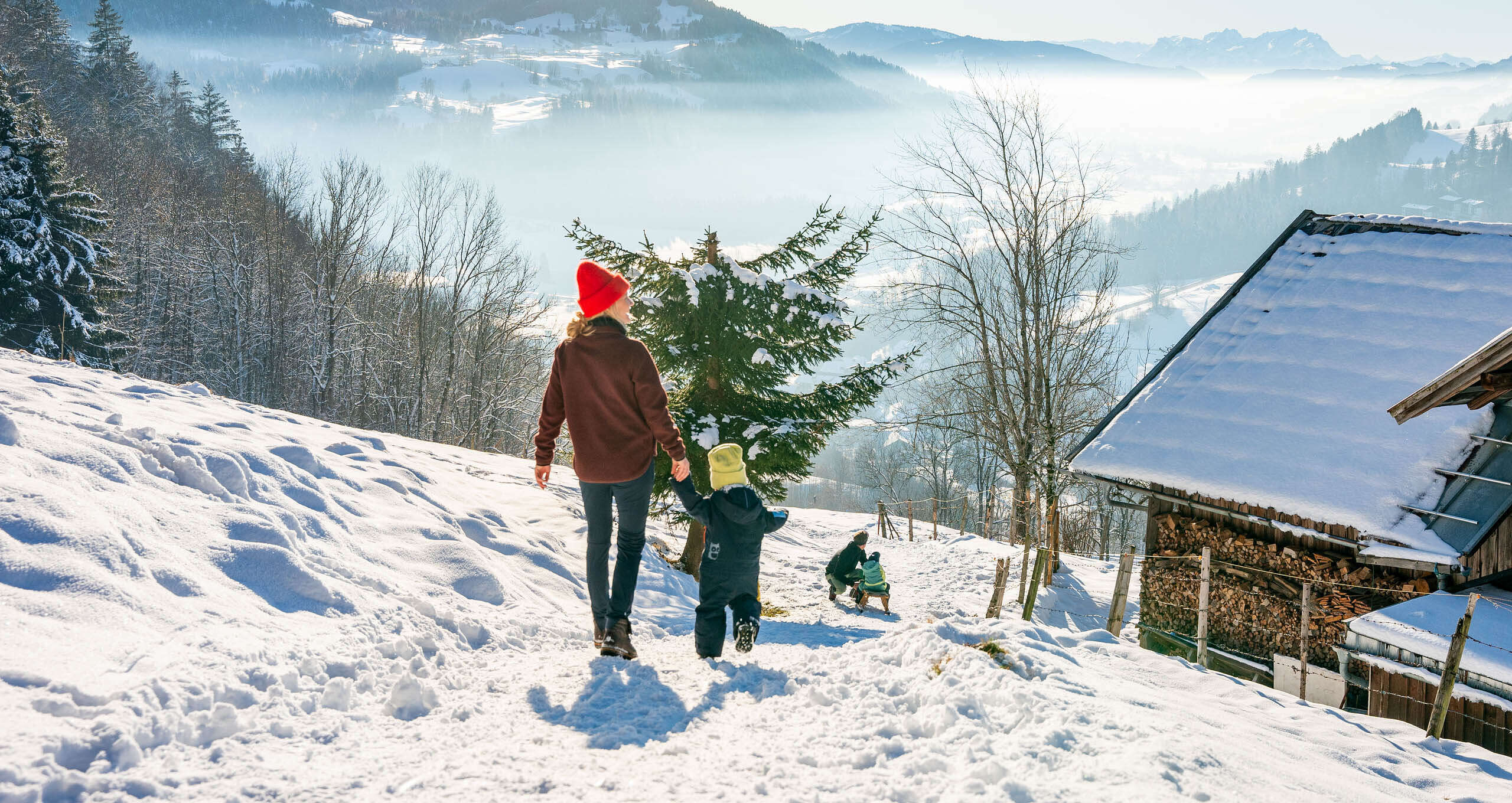 Familienwandern mit Schlittenfahrt am verschneiten Staufen in der Wintersonne mit Weitblick auf die Berge von Oberstaufen