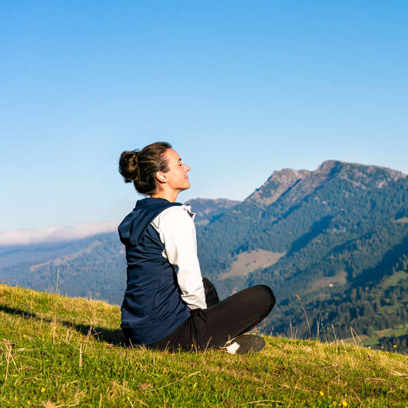 Frau sitzt im Gras mit geschlossenen Augen und genießt. Im Hintergrund Bergpanorama der Nagelfluhkette.,