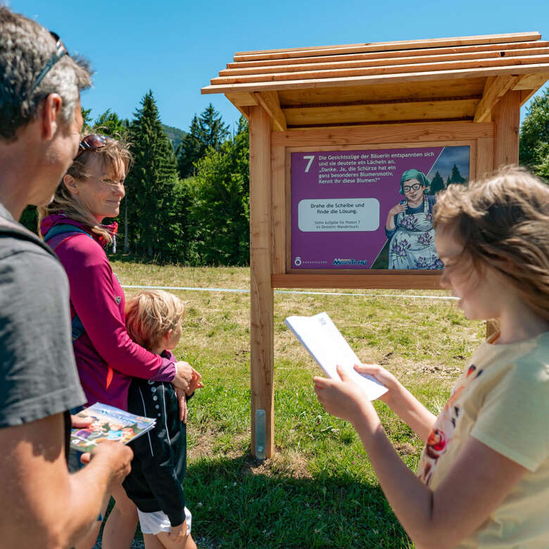 Familie beim Rätselraten an Station 7 auf dem Mounteensweg