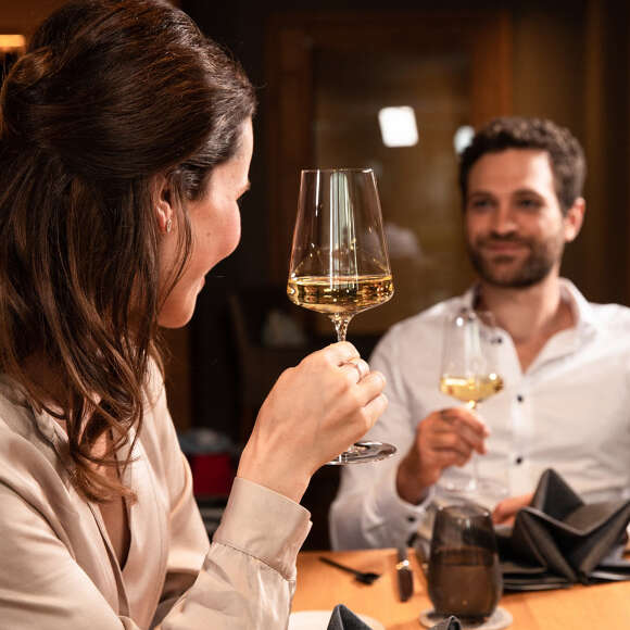 Paar beim Essen in einem Restaurant in Oberstaufen beim Astoßen mit einem Glas Weißwein.