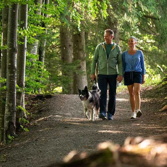 Pärchen wandert mit ihrem Hund durch den Wald in Oberstaufen