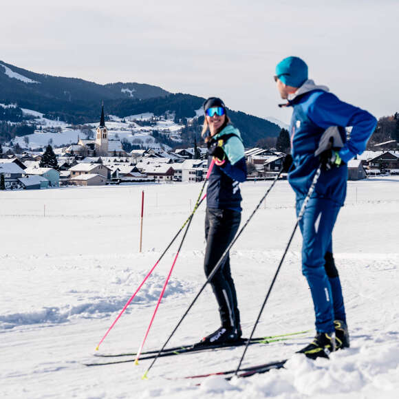 Langläufer stehen auf der Loipe bei Kalzhofen mit Blick auf Oberstaufen im Schnee.