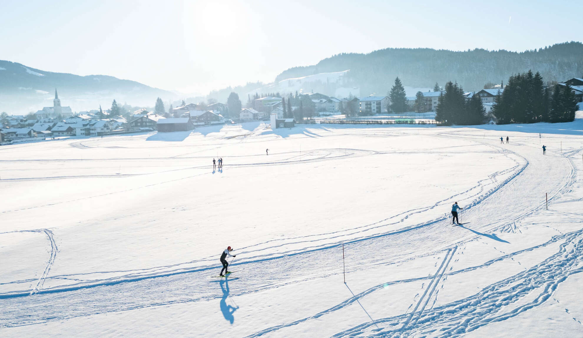 Langlaufen auf der Kalzhofer Loipe bei strahlender Wintersonne und Ortspanorama von Oberstaufen