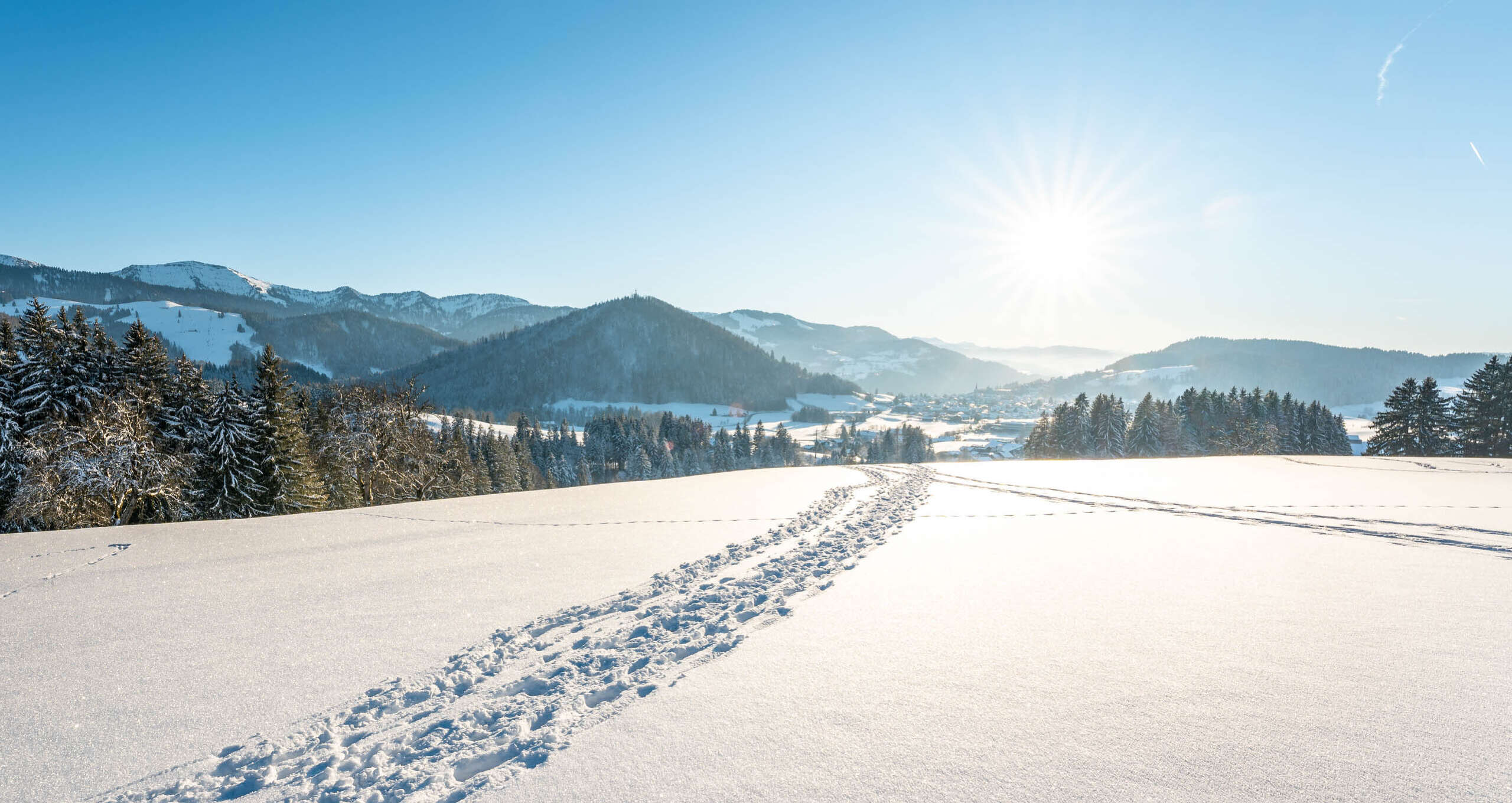 Spuren von Schneeschuhen in verschneiter Natur mit Ausblick auf den Staufen und Berge von Oberstaufen